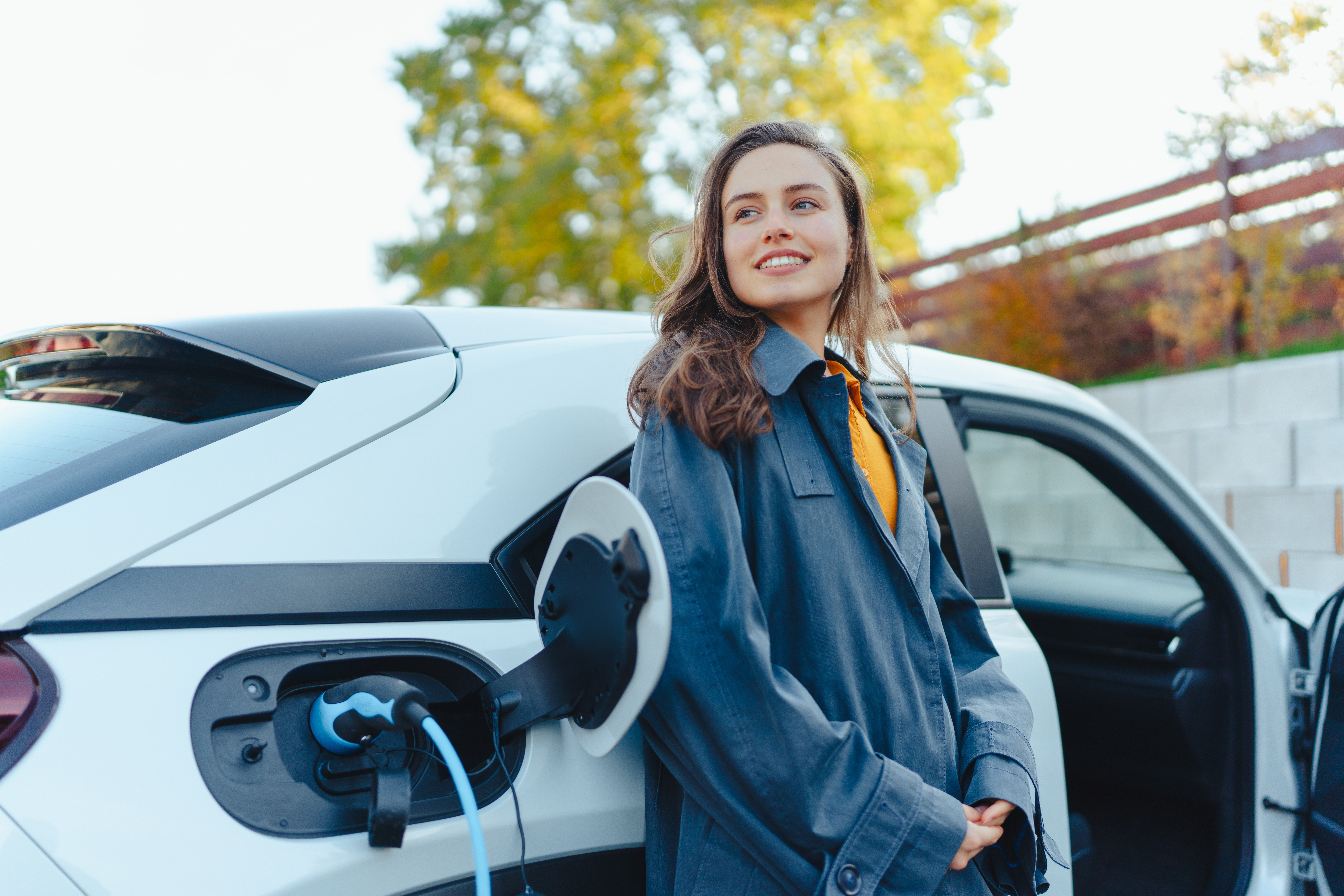 Eine junge Frau steht neben einem Elektroauto, während dieses geladen wird. Symbolbild.