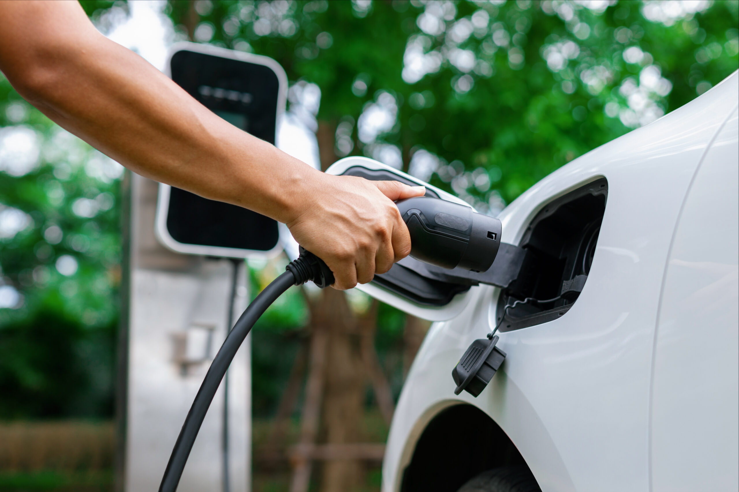 Focus hand insert progressive EV charger plug to EV car with blur background.